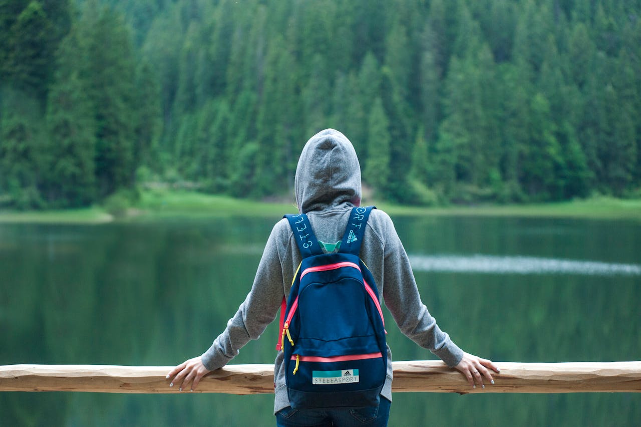 digital A person in a hoodie stands by a serene lake surrounded by lush greenery, enjoying the peaceful outdoors.