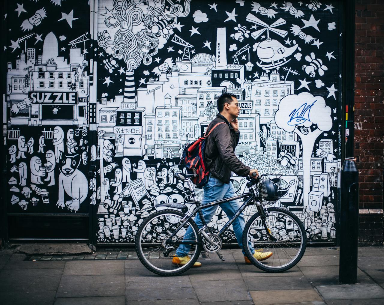 creative Man walking a bicycle past a detailed urban graffiti mural in a city setting.